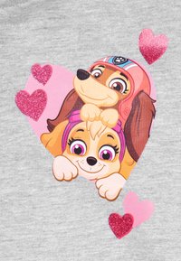 Il design della maglietta presenta due cani fumettistici all'interno di un cuore rosa, accentuato da cuori rosa glitterati su uno sfondo grigio.