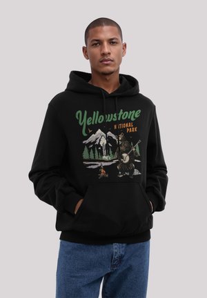 Schwarzer Hoodie mit einem Grafikdruck eines Bären, der Banjo spielt, umgeben von Bergen und Bäumen, beschriftet mit "Yellowstone Nationalpark". Weicher Stoff.