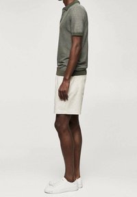 Polo rayé gris et blanc, short beige à taille élastique, et baskets blanches. La vue de côté montre une coupe décontractée et des manches courtes.