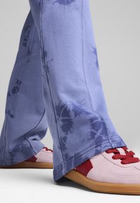 Gaišzilas šūnu zīmējuma bikses, izgatavotas no mīksta auduma; tām ir brīvā piegriezuma stils. Valkātas kopā ar sarkaniem un rozā sporta apaviem ar gumijas zoli.