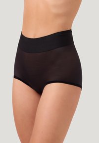 Vrouw in hoge zwarte doorschijnende onderbroek met brede tailleband, die torso en bovenbenen toont tegen een neutrale achtergrond.