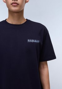Marineblå bomulds t-shirt med korte ærmer og et lille grafisk logo på venstre brystområde. Glat tekstur og normal pasform.