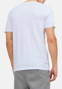 Hvid bomulds T-shirt med korte ærmer, rund hals og en glat tekstur; vist fra bagsiden, parret med grå bukser.