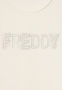 T-shirt color crema con la scritta "FREDDY" contornata da piccole strass lucenti, creando un design testurizzato e scintillante.