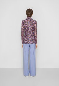 Długa koszula z kwiatowym wzorem w ciemnym purpurze, połączona z jasnoniebieskimi spodniami szerokimi. Gładki materiał o dopasowanym kroju.