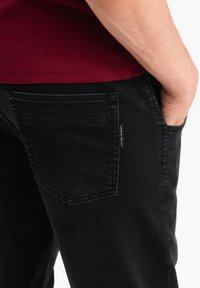 Svarta denimjeans med en figurnära passform, som har en bakficka med sömnadsdetaljer och en liten märkesetikett på sidan.