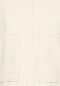 Krémová bunda s textúrou, ktorá obsahuje vzorované tkanivo s viditeľným prešívaním, dva predné našité vrecká a jednoduchý otvorený dizajn.