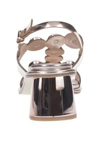 Sandalo metallico rosa pallido con tacco a blocco, caratterizzato da un design con ritagli e accenti circolari, realizzato in pelle liscia e con cinturini trasparenti.