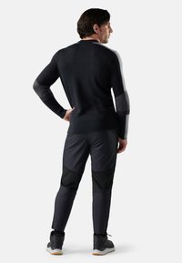 Zwart en grijs gebreid sweater met een aansluitend ontwerp, en donkere sportbroek met verschillende texturen en accenten. Gedragen met sportchoenen.