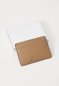 Rudos odos kortelių laikiklis su iškaustytu „MICHAEL KORS“ logotipu, turintis keturias kortelių kišenes ir minimalistinį dizainą. Supakuota.