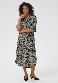 Robe mi-longue à manches courtes, en imprimé léopard beige avec des taches noires. Elle présente un décolleté en V et une silhouette ample et fluide.