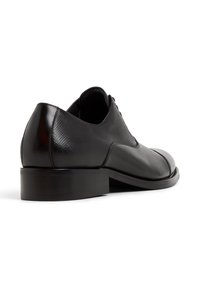 Scarpa di pelle nera con una texture liscia, tacco basso, punta arrotondata e dettagli sottili lungo il lato e la parte superiore.