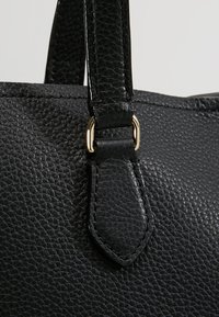 Zwarte lederen handtas in close-up, met een gestructureerd oppervlak, stevige handgreep met gestikte details en een goudkleurig hardwareaccent.