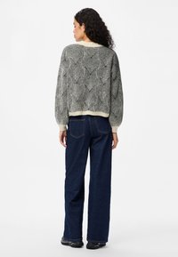 Gestrickter Pullover mit einem strukturierten Schwarz-Weiß-Muster, mit Rundhalsausschnitt und geripptem Saum. Kombiniert mit dunkelblauen weit geschnittenen Jeans.