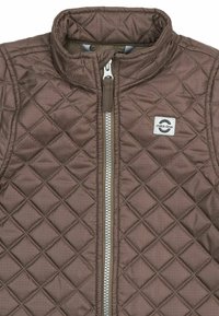 Veste marron matelassée avec une couture en losange, une fermeture éclair centrale argentée et un petit patch logo rectangulaire blanc "mikk-line" sur la poitrine gauche.