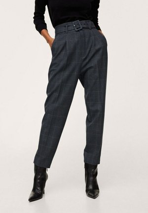 Woman wearing high-waisted grey checked trousers with a matching belt, black long-sleeve top, and black pointed heeled ankle boots.