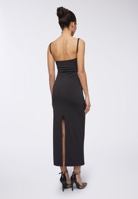 Abito maxi nero senza maniche con una silhouette aderente, caratterizzato da uno spacco sul retro e una texture liscia. Abbinato a tacchi alti neri e dettagli con stampa animale.