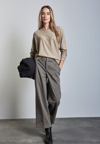 Maglione beige a maniche lunghe abbinato a pantaloni larghi a scacchi e stivaletti neri alla caviglia. Accessorio: giacca imbottita nera arrotolata sotto il braccio.