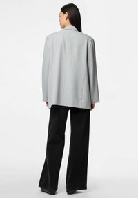 Gaiši pelēks pārāk liels žakets ar strukturētām plecu daļām, garām piedurknēm un gludu tekstūru, apvienots ar melniem izplestos biksēm.