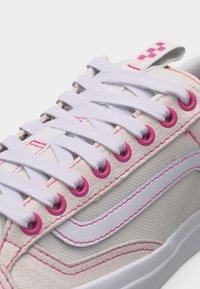 Κοντινό πλάνο λευκού αθλητικού παπουτσιού με ροζ τρύπες για τα κορδόνια, λευκά κορδόνια, ροζ ραφές και λευκή λωρίδα στο πλάι πάνω σε υφασμάτινο επάνω μέρος με υφή.