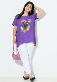 T-shirt violet avec un graphique d'un chien portant des lunettes de soleil et des écouteurs; associé à un pantalon blanc et un sac à main rose scintillant.