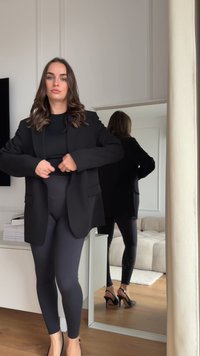 Svart oversized blazer med glatt tekstur, båret over en tettsittende svart topp og mørke leggings. Inkluderer høye hæler og speilrefleksjon.