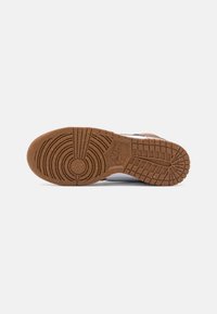 Sneaker sole with a textured gum rubber surface featuring circular and grid patterns. White upper material visible along the edges.