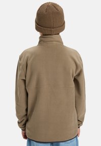 Veste en polaire marron avec un col montant et une coupe décontractée, affichée de dos. Elle présente des manches longues et un tissu texturé.