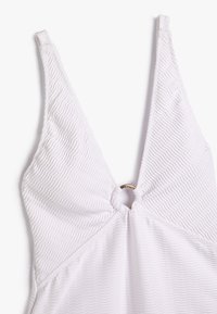 Witte ééndelige zwemkleding met een V-hals, textuur met golven en een ronde gouden ringaccent in het midden van de buste.