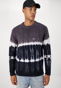 Pull en polaire avec un col rond, présentant un motif dégradé tie-dye dans des nuances de gris, marine et blanc. Manches longues et texture douce.