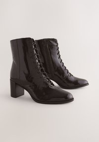 Sorte ankelstøvler i laklæder med spids snude, høj blokhæl, snørebånd foran og lynlås i siden.