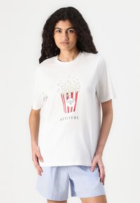 T-shirt in cotone bianco con grafica di un secchio di popcorn a strisce rosse e popcorn bianchi, testo "ATTITUDE" e maniche corte.
