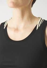 Svart linne med rund halsringning, tillverkat av texturerat svart tyg och med ljusa randiga accenter på axelbanden.