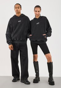 Svarte oversized hettegensere med et spirallogo, kombinert med svarte vide jeans og tettsittende sykkelshorts. Svarte knelange platåstøvler.