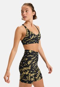 Sports bra and high-waisted shorts set, black with green abstract patterns and purple accents. Fabric is stretchy with a smooth texture.