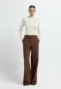 Witte geribde turtleneck trui gecombineerd met hooggeroeide, wijdvallende bruine broeken. Soepele textuur en een getailleerde pasvorm, met zijzakken.