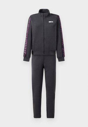 Tummanharmaa verryttelyasu, jossa on vetoketjullinen takki, jossa on purppurat logot kuvioina hihoissa ja yhteensopivat slim-fit housut. Pehmeä kangas, jolla on sileä rakenne.