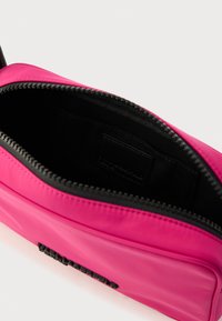 Rózsaszín, sima anyagból készült táska. Fekete cipzárral és belső fekete béléssel rendelkezik, melyen egy kis címke található. Kompakt kialakítás.