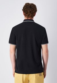 Czarna koszulka polo z krótkimi rękawami, z białymi paskami na kołnierzyku i rękawach. Gładka tekstura i luźny krój.