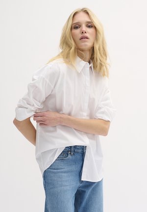 White button-up shirt with rolled sleeves, made of cotton, paired with light blue denim jeans. The shirt has a loose, relaxed fit.