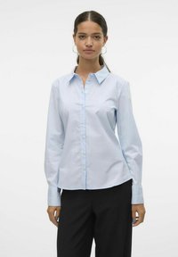 Camisa de botón de manga larga azul claro hecha de mezcla de algodón. Presenta un cuello clásico y un dobladillo curvado, con una textura suave y un acabado blando.