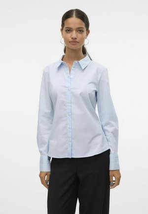Camisa de botón de manga larga azul claro hecha de mezcla de algodón. Presenta un cuello clásico y un dobladillo curvado, con una textura suave y un acabado blando.