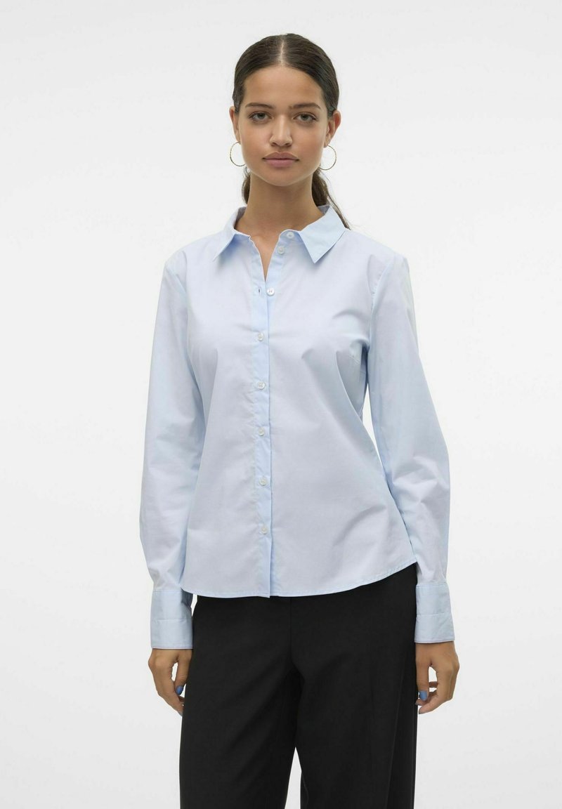 Camisa de botón de manga larga azul claro hecha de mezcla de algodón. Presenta un cuello clásico y un dobladillo curvado, con una textura suave y un acabado blando.