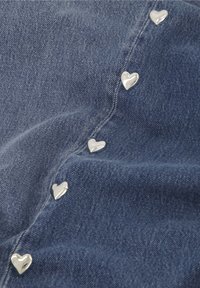 Denim stof in donkerblauw met een gladde textuur, met zilveren hartvormige hardwareaccenten langs de naad.