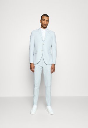 Light blue linen suit with a tailored fit, featuring a single button closure and notch lapels, paired with white sneakers.