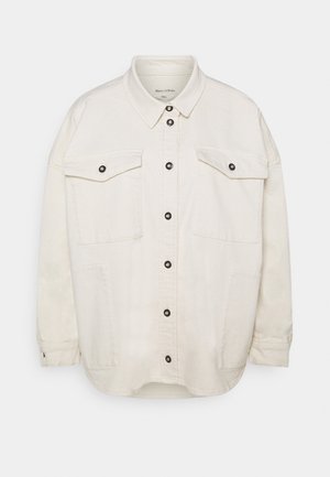 Beige suurendatud särk-jakk, mis on valmistatud puuvillast, nööpidega esiosaga, kahe rinnataskuga ning mustade klõpsnuppudega. Omab pikki varrukaid ja ümmargust serva.