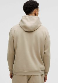 Vaahto beige huppari, jossa on suuri huppu, pehmeä rakenne, pitkät hihat ja rento leikkaus. Ribbattu hihansuut ja helma, minimaalinen muotoilu.