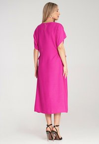 Rosa Midikleid mit kurzen Ärmeln, rundem Ausschnitt, Schlüssellochverschluss auf der Rückseite und Kordelzug in der Taille. Kombiniert mit schwarzen Riemchen-Heels.