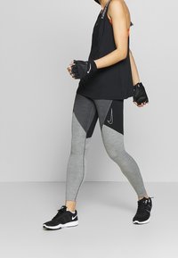 Czarny top na ramiączkach, legginsy w szarym i czarnym wzorze oraz czarne buty sportowe. Strój charakteryzuje się materiałem odprowadzającym wilgoć oraz dopasowanym krojem.