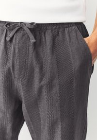 Gray textured pants with a drawstring waist, featuring side pockets and a vertical stripe pattern in a lightweight fabric.